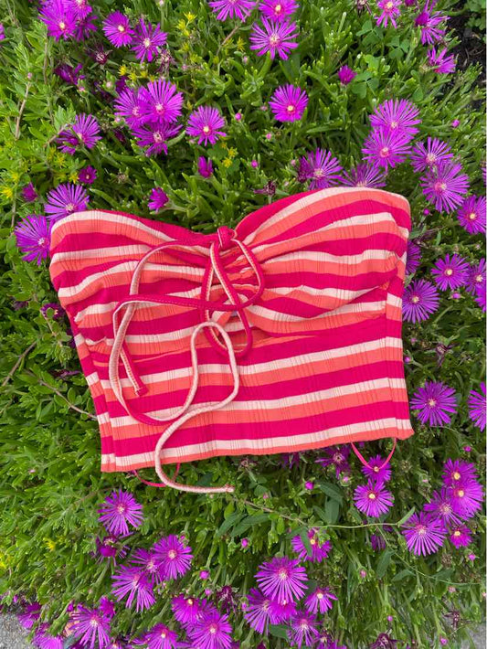 Pink and red striped strapless crop top with front lace-up detail, laid on purple flowers.