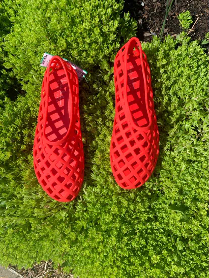Red woven ballet flats with rounded toes and small pull tabs on green grass background.