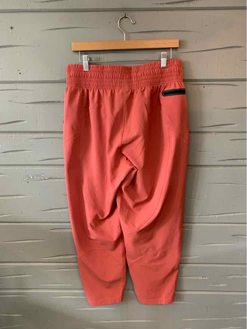 Coral red Under Armour jogger pants with elastic waistband and zippered pocket on right side.