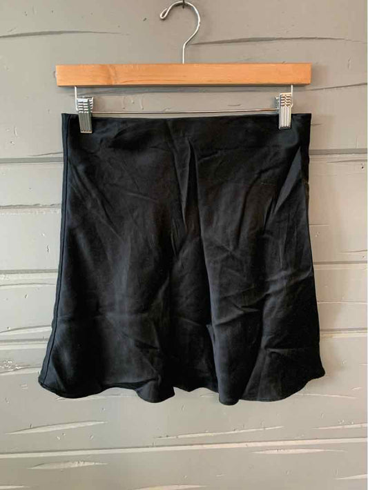 Black medium skirt with flared hem hanging on wooden hanger against gray wall.