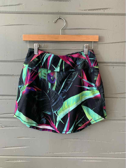 Black women’s shorts with vibrant neon green, pink, and blue abstract leaf pattern, size small, hanging on wooden hanger.