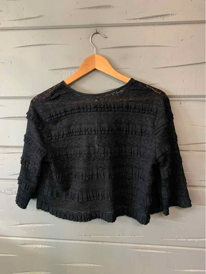 Black long-sleeve lace top with a sheer textured pattern and scalloped hem, hung on a wooden hanger.