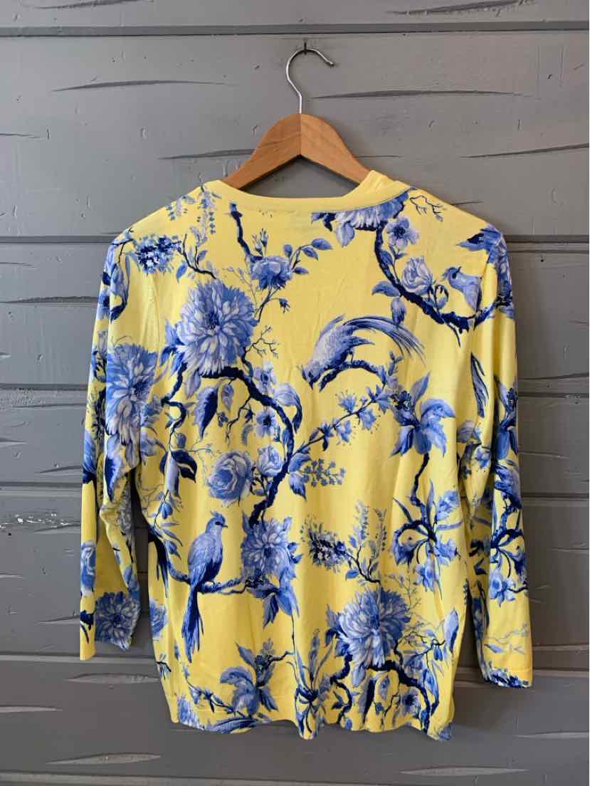 Yellow long-sleeve blouse with blue floral print and gathered hem, hanging on wooden hanger.