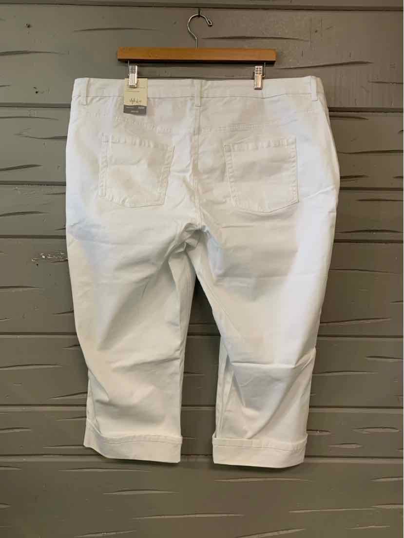 White cropped pants with back pockets and belt loops hanging on wooden hanger against gray wooden wall.