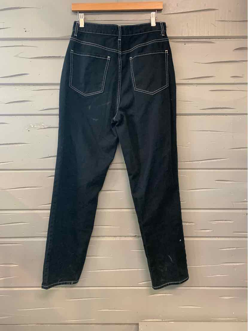 Black high-waisted straight-leg jeans with back pockets hanging against a gray wooden wall.