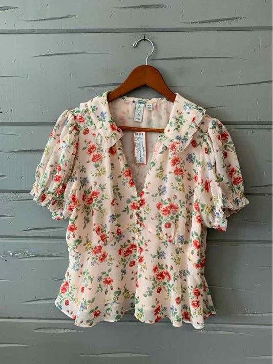 Light pink floral blouse with puff sleeves and a ruffled collar on wooden hanger.