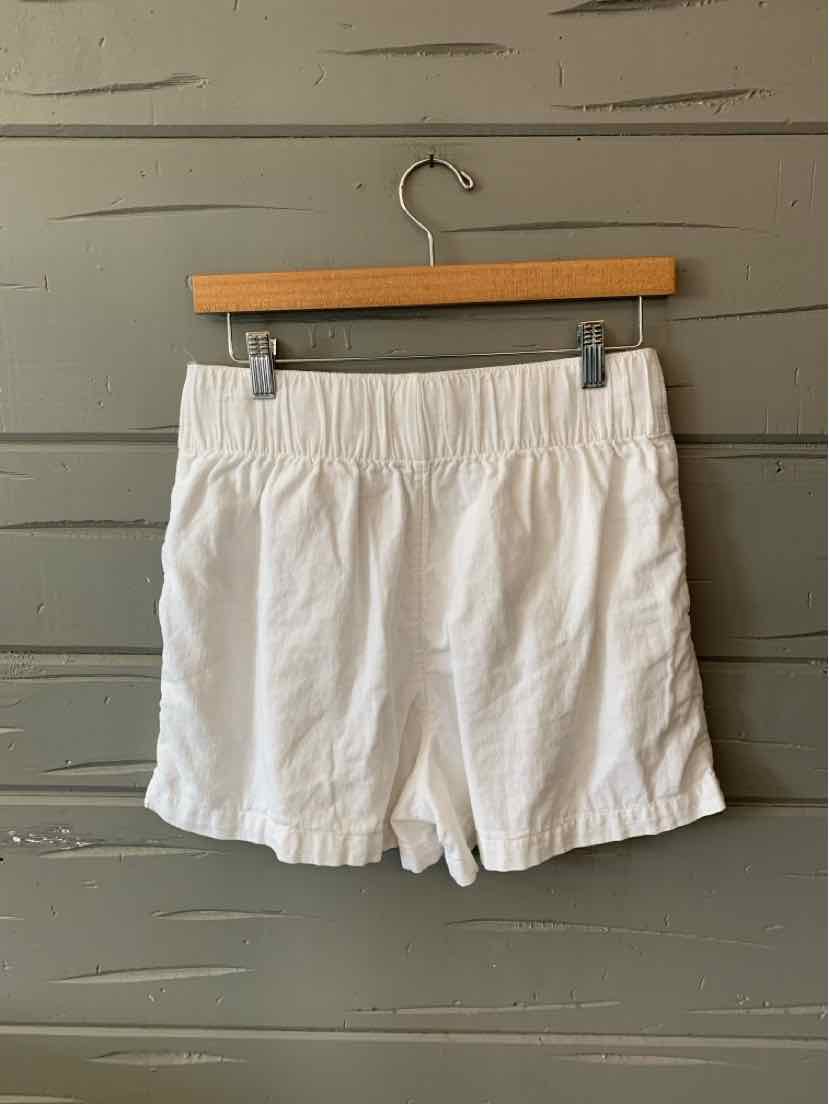 White casual shorts with elastic waistband and a relaxed fit hanging on wooden hanger.