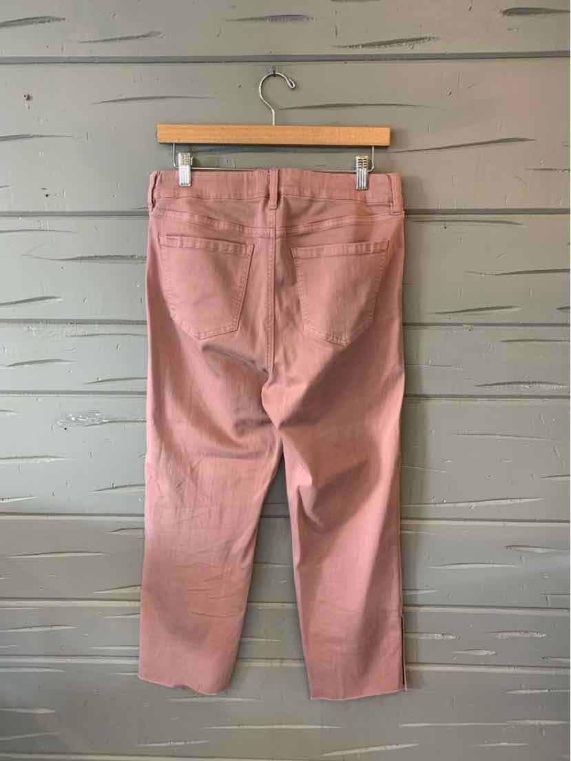 Pink straight-leg pants with back pockets hanging on wooden hanger against gray wooden wall.