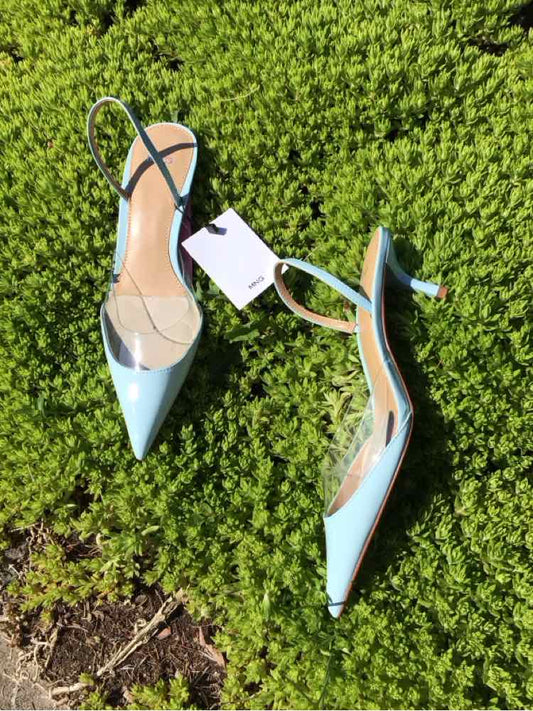 Light blue pointed-toe slingback heels with transparent side panels and low kitten heels on green grass background.