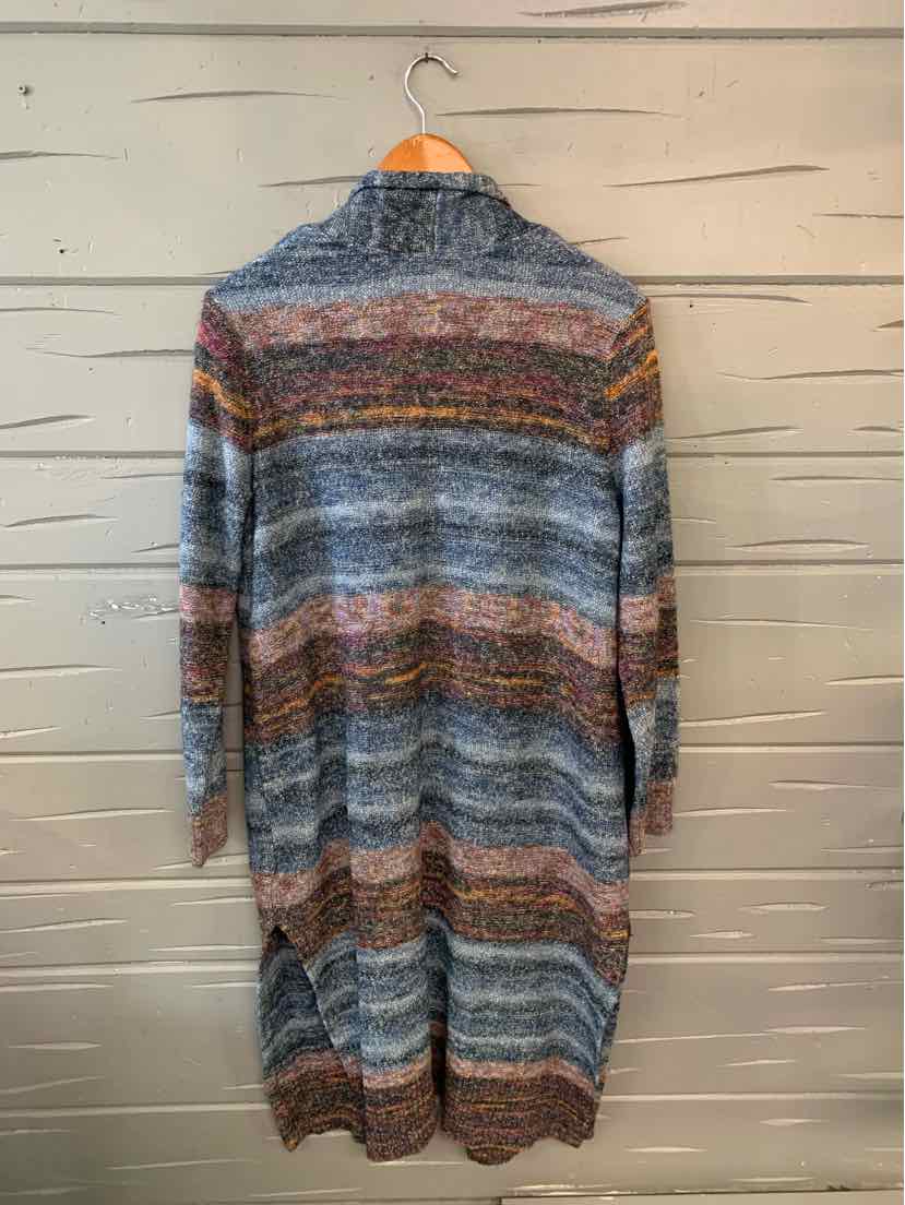 Long striped cardigan with blue, brown, gray, and rust tones hanging on wooden wall.