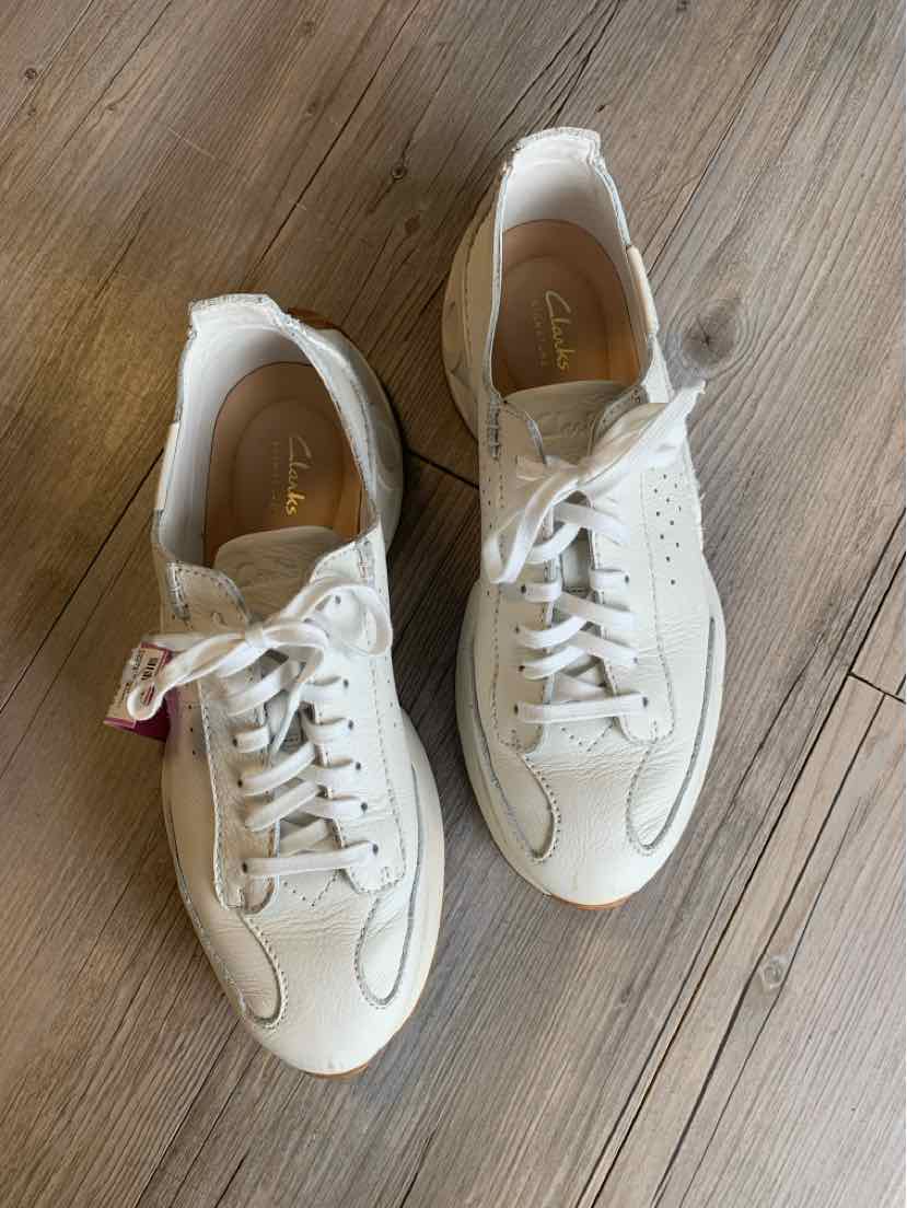 White leather Clarks sneakers with laces and stitching details on wooden floor, size 10.