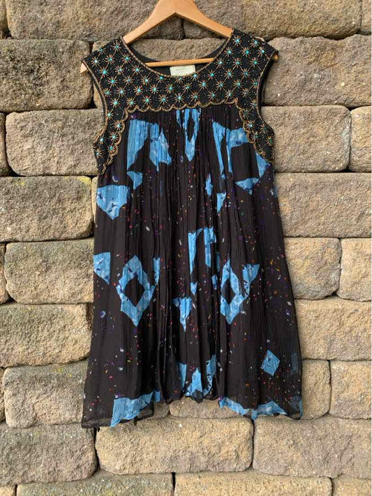 Black sleeveless dress with blue geometric patterns and beaded neckline on wooden hanger.