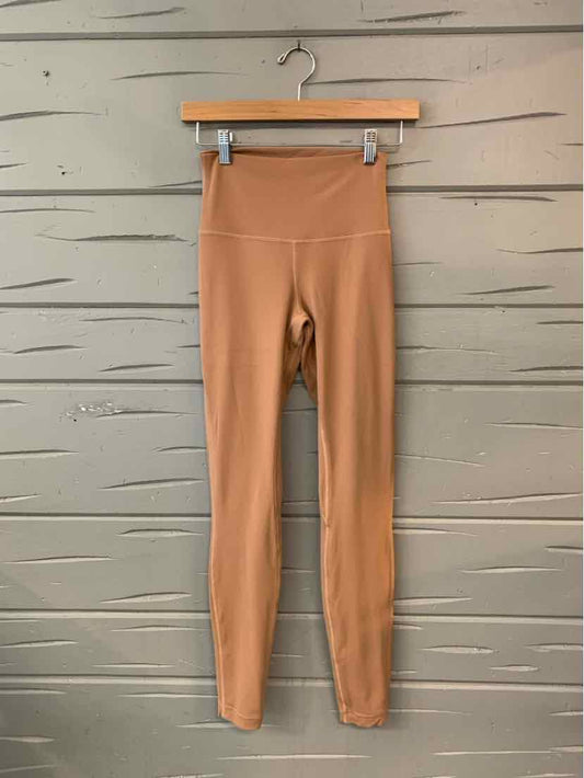 High-waisted tan leggings with wide waistband and smooth, stretchy fabric hanging on wooden hanger.