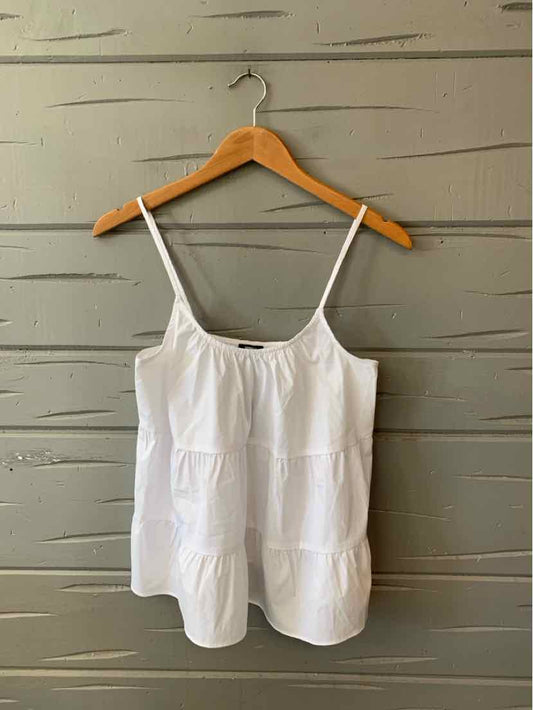 White sleeveless tiered camisole with adjustable spaghetti straps on wooden hanger.