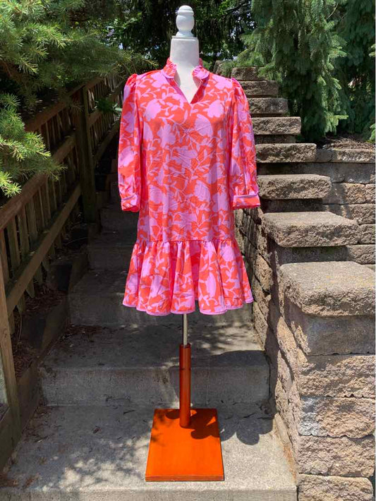 Pink floral dress with long sleeves, V-neck, and ruffled hem displayed on mannequin outdoors.