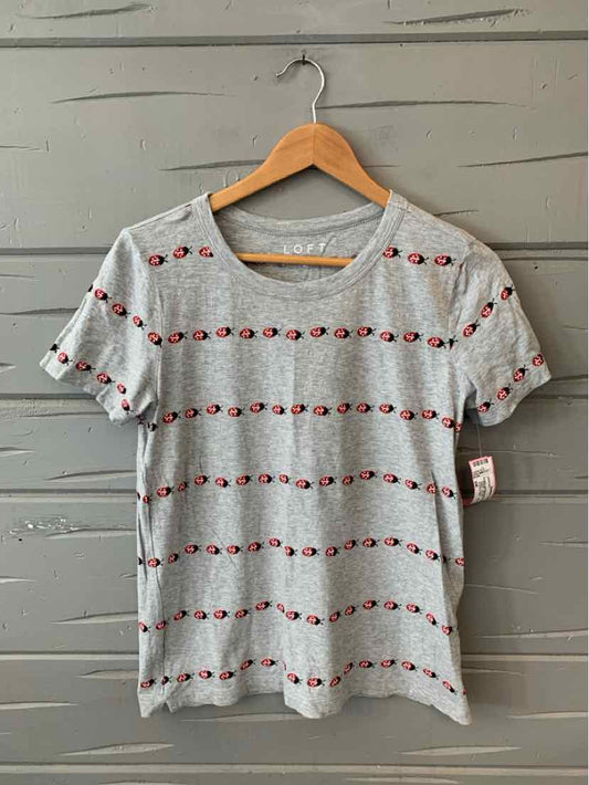 Light gray short-sleeve T-shirt with horizontal rows of small red and black ladybug prints, round neckline.