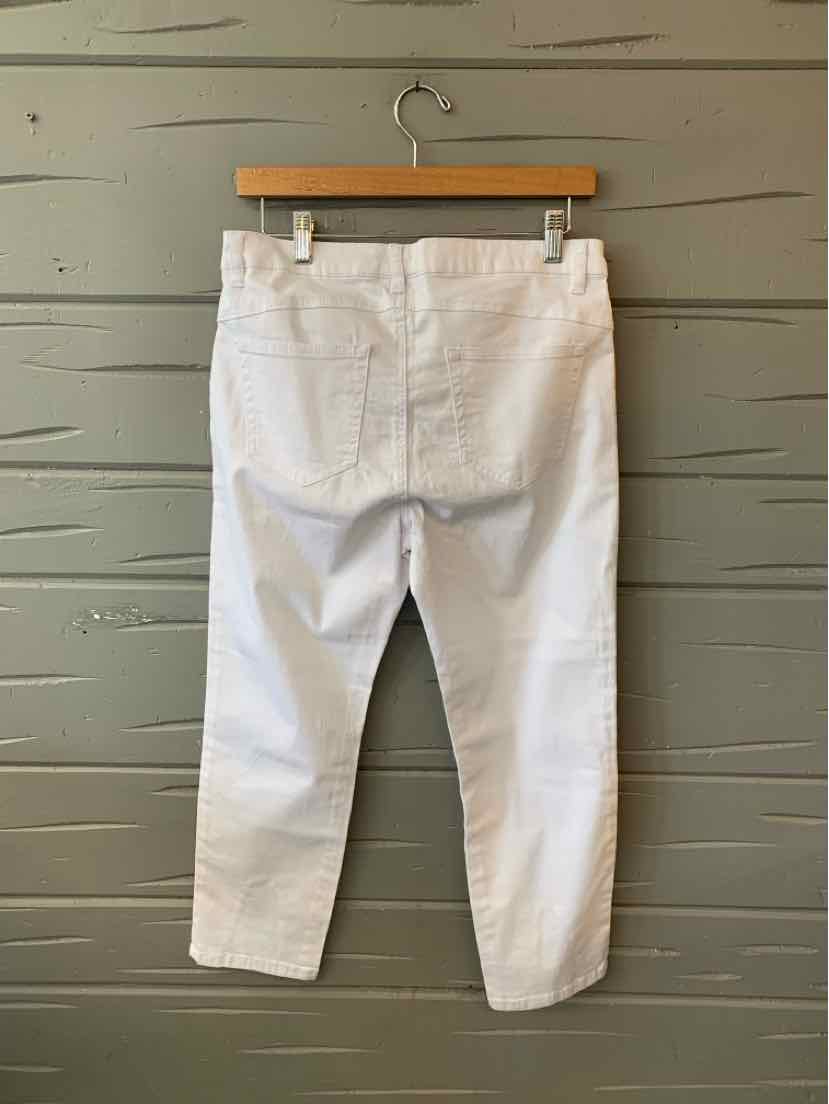 White cropped pants with back pockets and seam details, hanging on wooden hanger against gray wall.