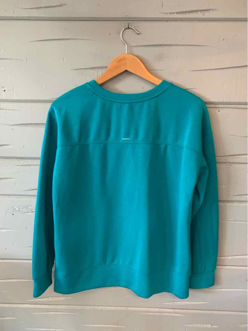 Teal long-sleeve crewneck sweatshirt with relaxed fit, hanging on wooden hanger against light wood wall.