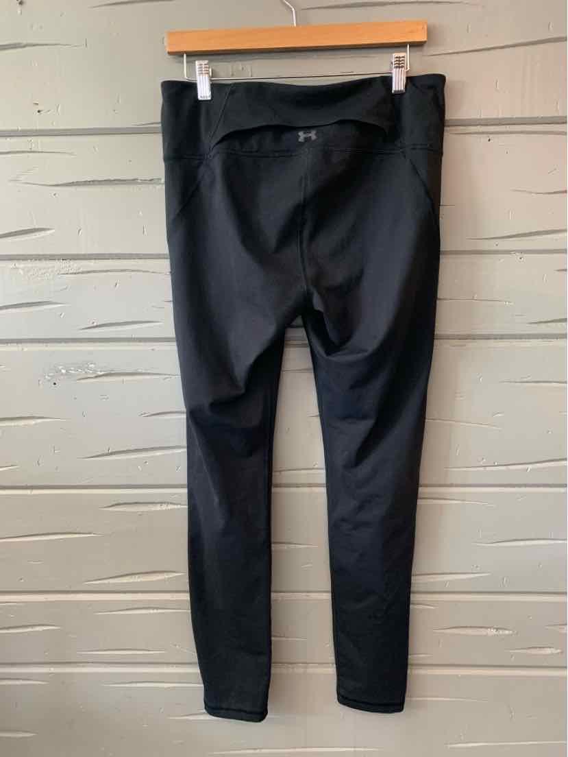Black women's Under Armour leggings in large size with back waist pocket hanging on wooden hanger.