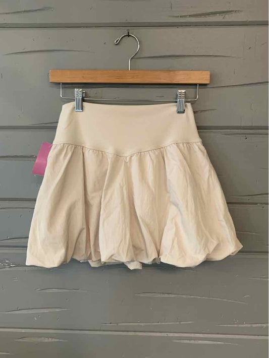 Beige skort with gathered, flowy skirt design and fitted waistband hanging on wooden hanger.