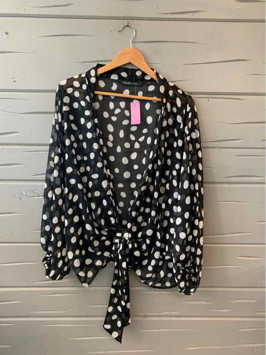 Black long-sleeve blouse with white polka dots and front tie detail on hanger.