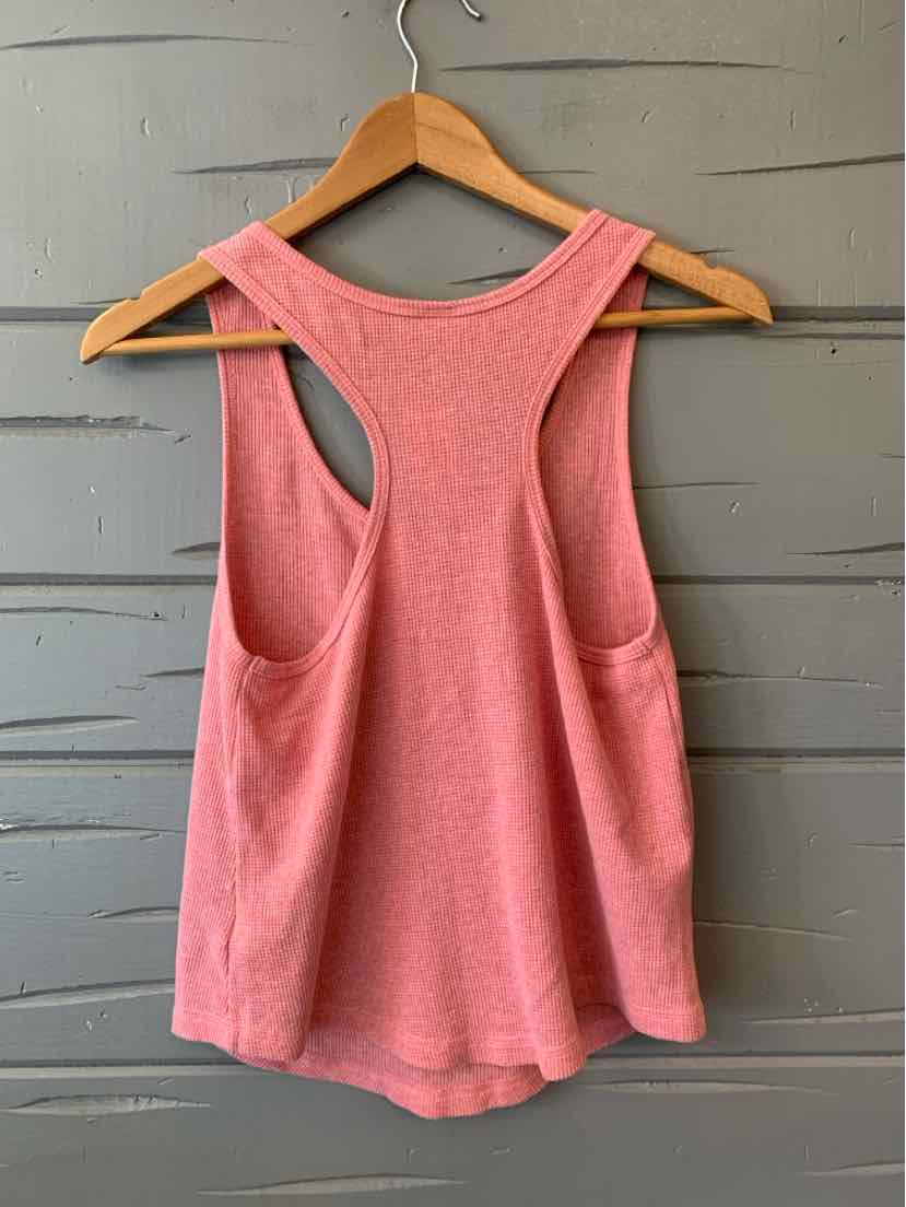 Pink sleeveless waffle-knit tank top with racerback hanging on wooden hanger against gray wall.