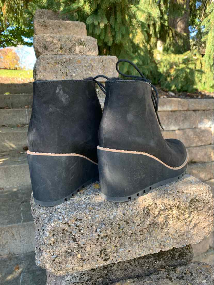 Pair of black leather ankle boots with rounded toes, low wedge soles, and thin tan welt trim.