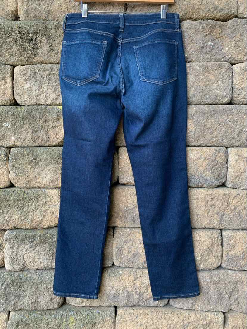 Dark blue denim jeans with straight legs and two back pockets hanging against stone wall background.