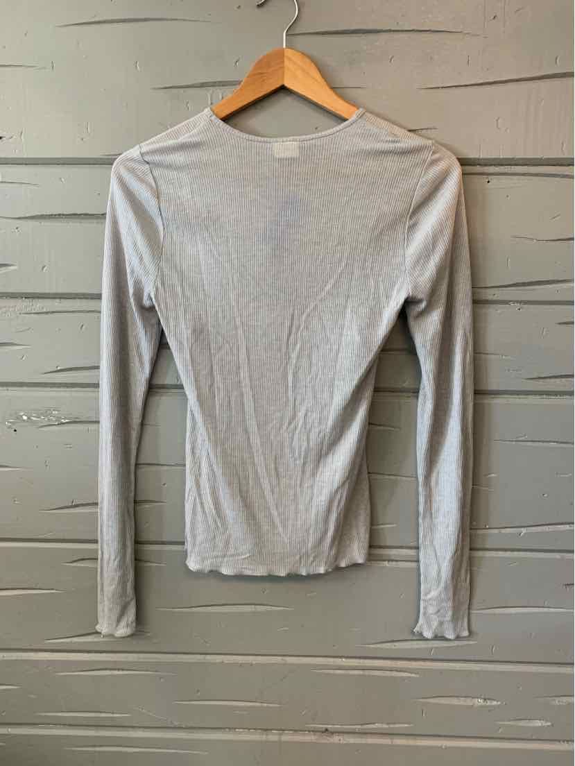 Light gray long-sleeve fitted crew neck shirt on wooden hanger against gray wall.