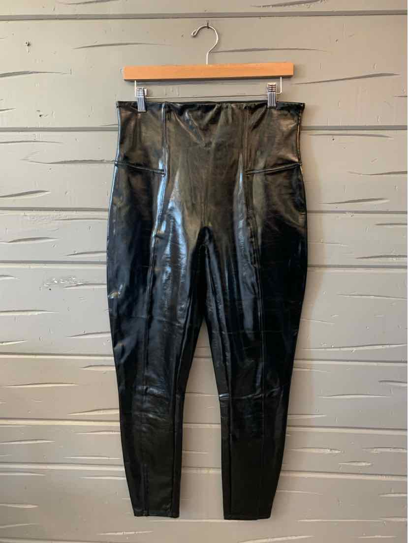 Black glossy faux-leather Spanx leggings with a high-rise waistband and slim legs, hanging on a clip hanger.