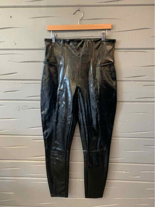 Black glossy faux-leather Spanx leggings with a high-rise waistband and slim legs, hanging on a clip hanger.