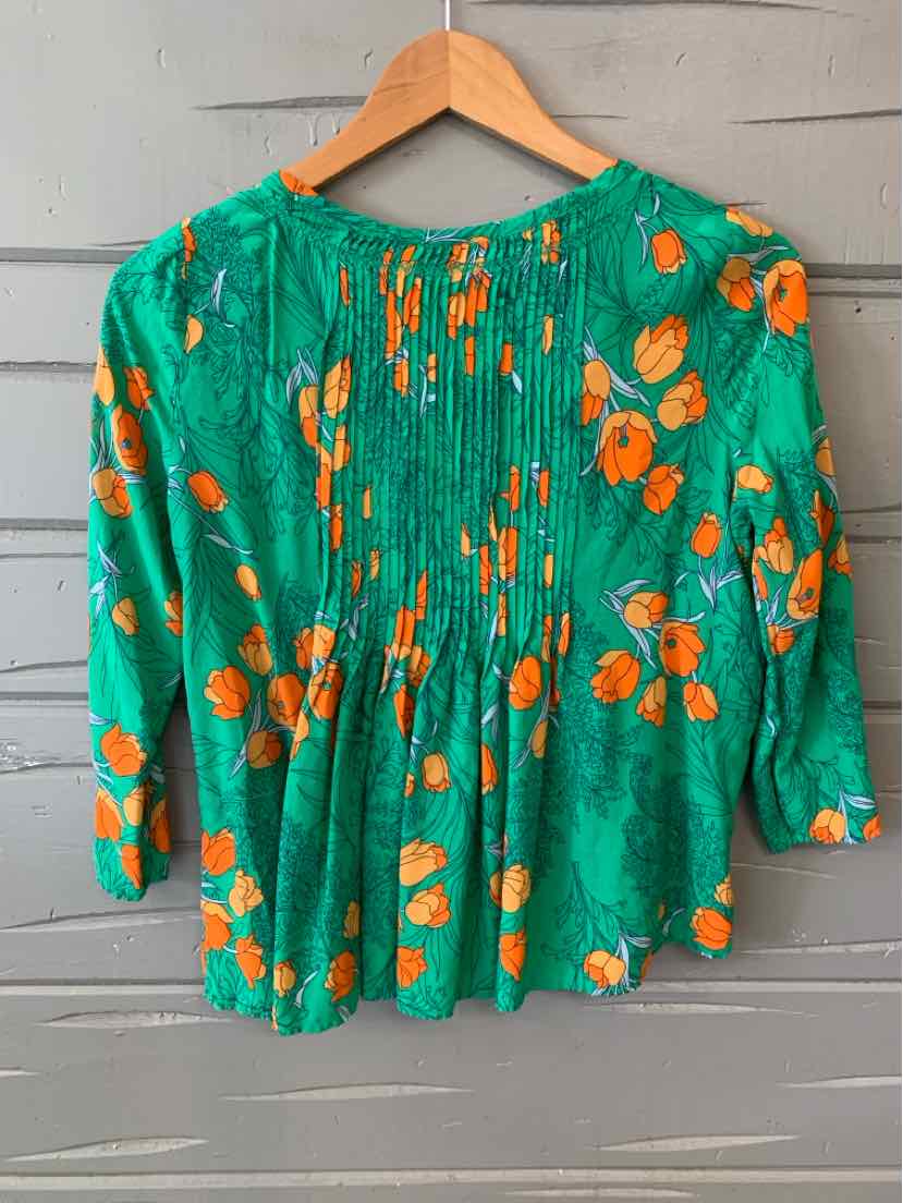 Green blouse with orange floral print, pintuck detailing, and three-quarter sleeves hanging on wooden hanger.