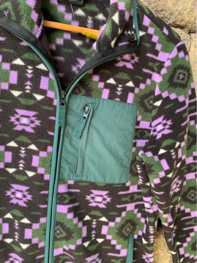 Fleece jacket with purple, green, and black Aztec pattern, featuring a green zippered chest pocket and teal zipper trim.