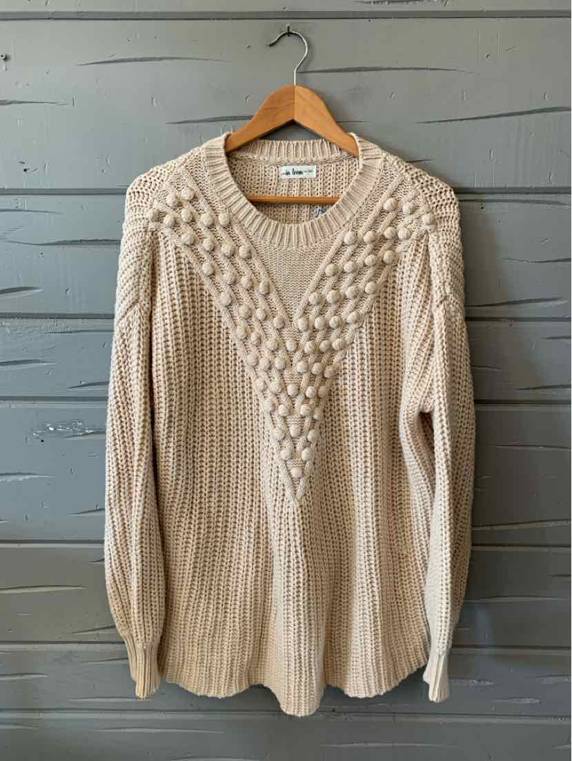 Oatmeal knit sweater with a V-neck, textured cable-knit front, and long sleeves hanging on a wooden hanger.