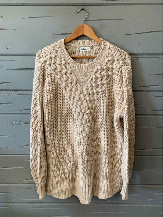 Oatmeal knit sweater with a V-neck, textured cable-knit front, and long sleeves hanging on a wooden hanger.