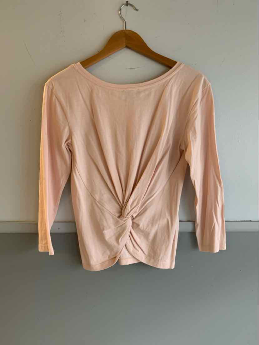 Light pink long-sleeve top with front twist detail and scoop neckline on wooden hanger.