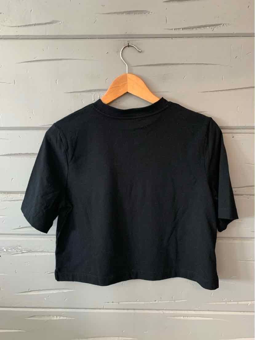 Black short-sleeve cropped t-shirt with crew neckline on wooden hanger against gray wall.
