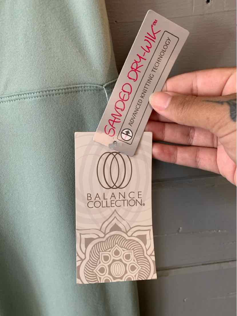 Light green garment tag with Balance Collection logo and "Sampled Drawing" label held by hand.