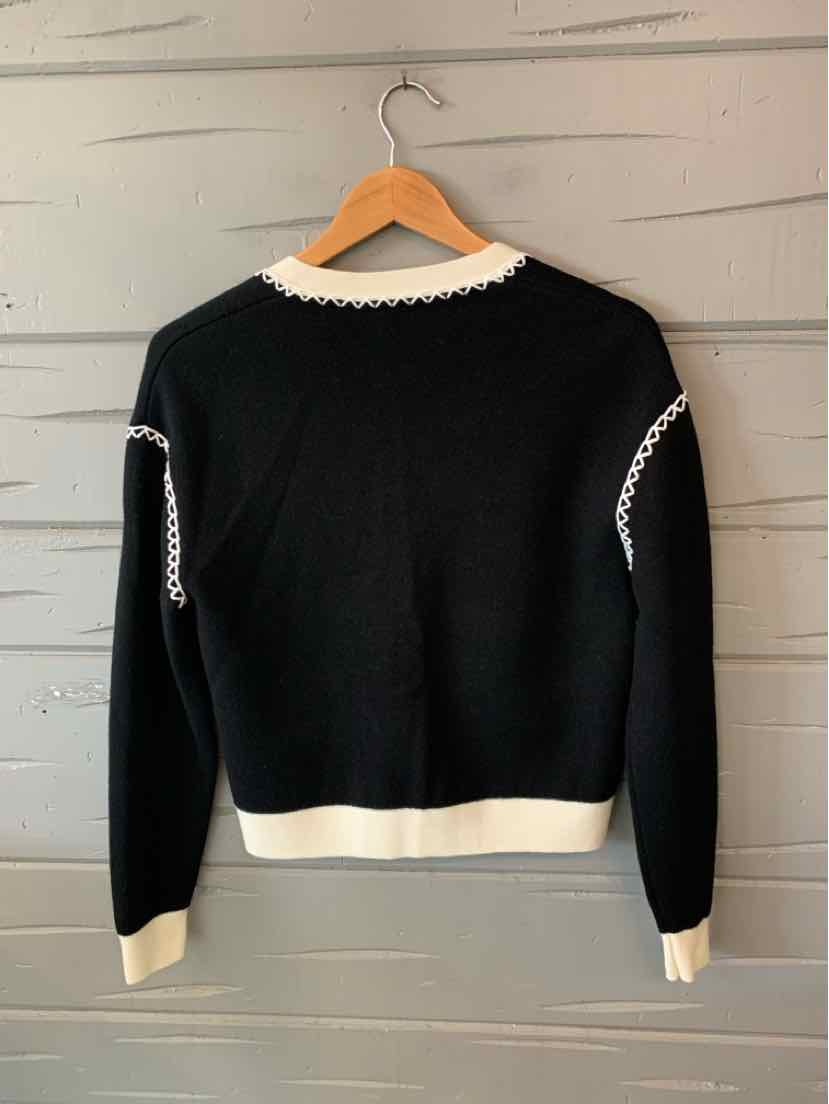 Black knit sweater with white trim at collar, cuffs, and hem, hanging on wooden hanger.