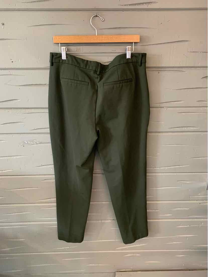 Olive green straight-leg pants with back welt pocket, hanging on wooden hanger against gray wall.