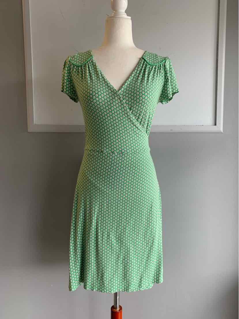 Green short-sleeve dress with white polka dots and a wrap-style V-neck on a mannequin.