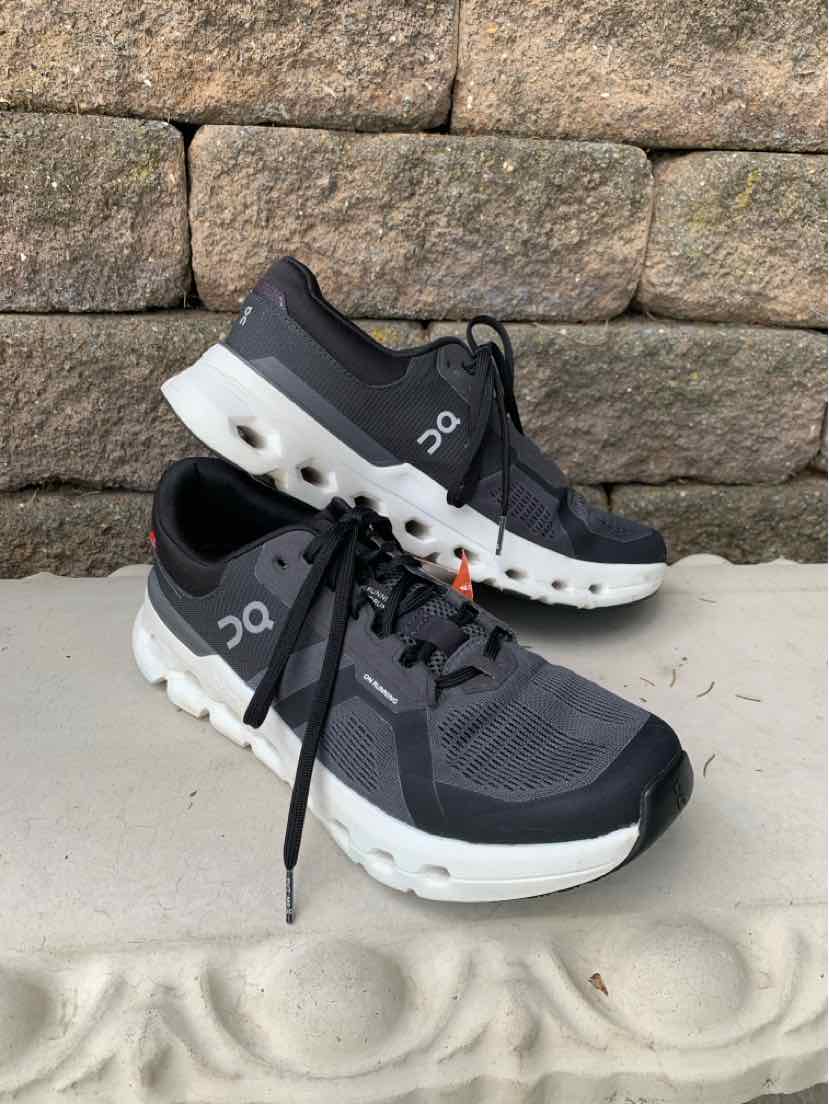 Black athletic sneakers with white cushioned midsoles featuring circular cutouts, mesh upper, and lace-up design.