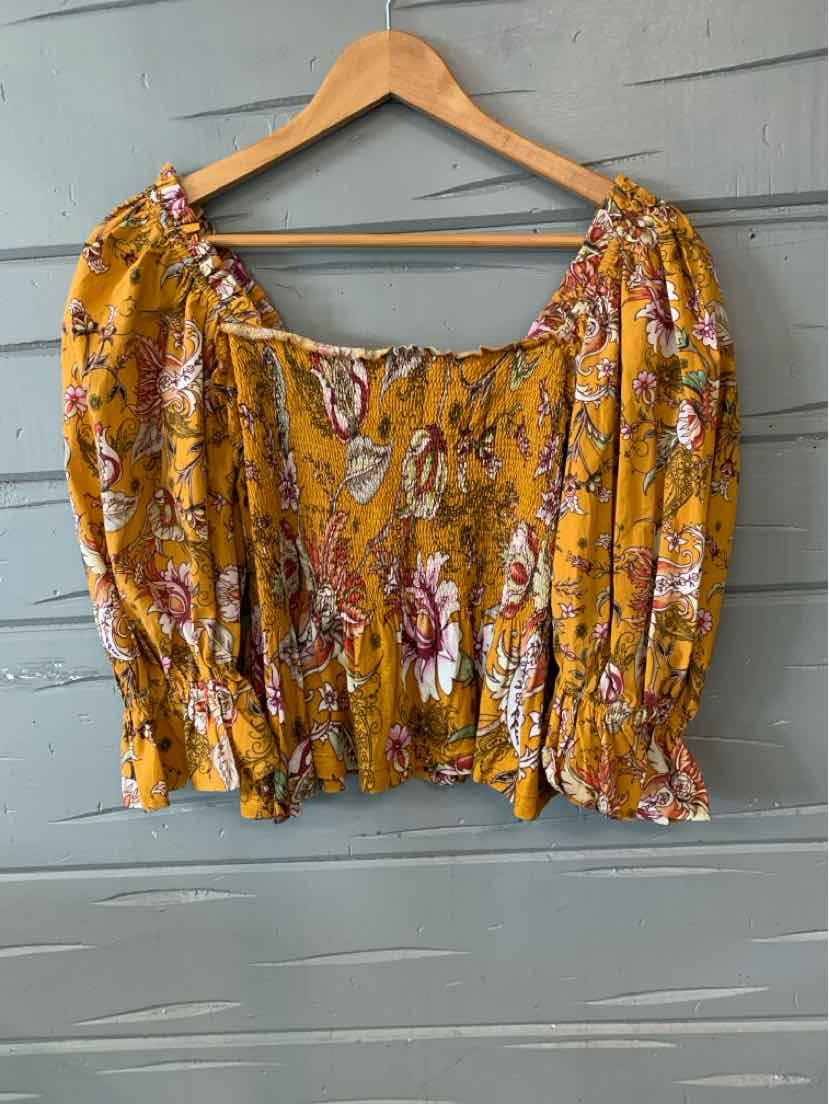 Yellow floral off-shoulder blouse with puffed long sleeves and smocked waist hanging on wooden hanger.