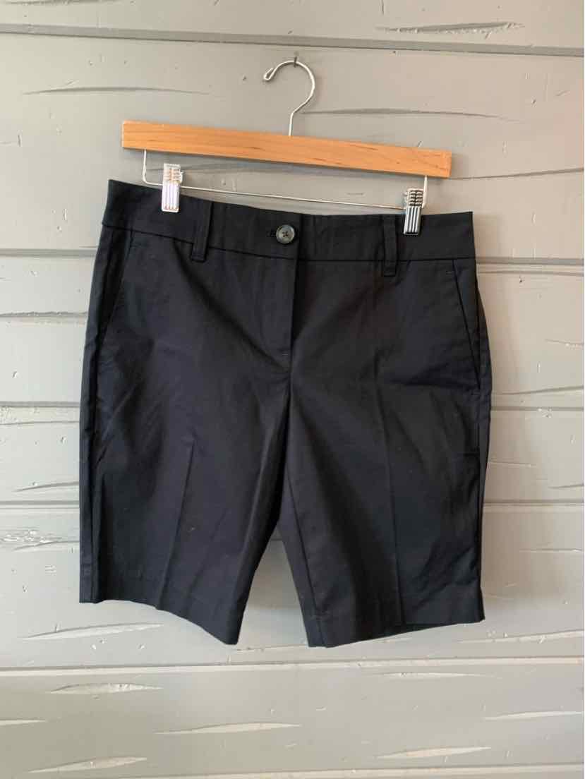 Black tailored knee-length shorts with front button and zip closure on wooden hanger.