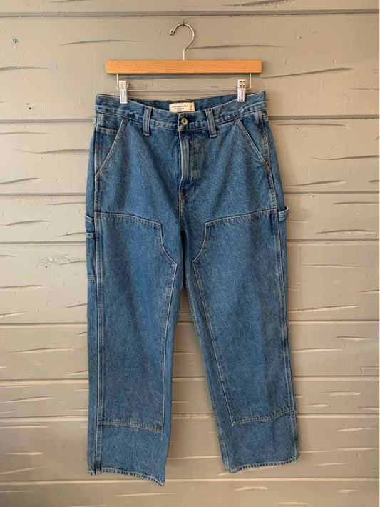 High-waisted blue denim jeans with relaxed fit and multiple seam details hanging on wooden hanger.