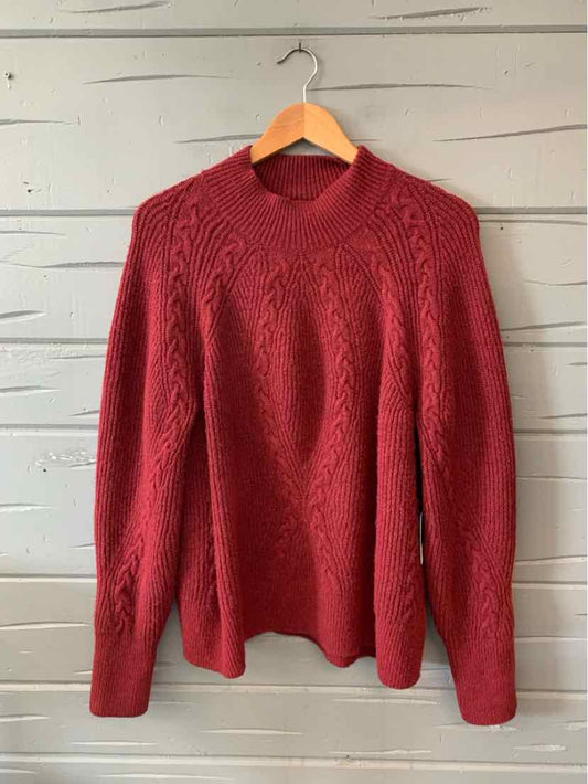 Long-sleeve red cable-knit sweater with crew neckline and fitted cuffs hanging on wooden hanger.