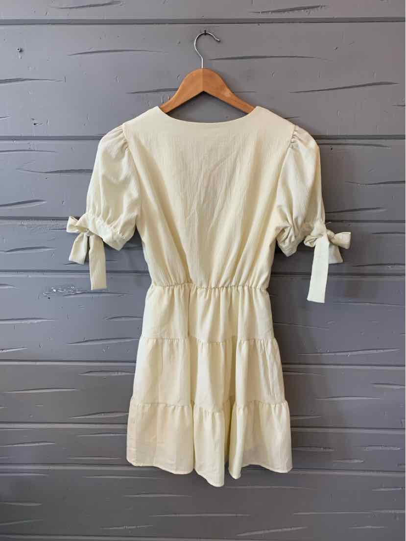 Cream-colored short dress with puff sleeves, cinched waist, and tied cuffs.