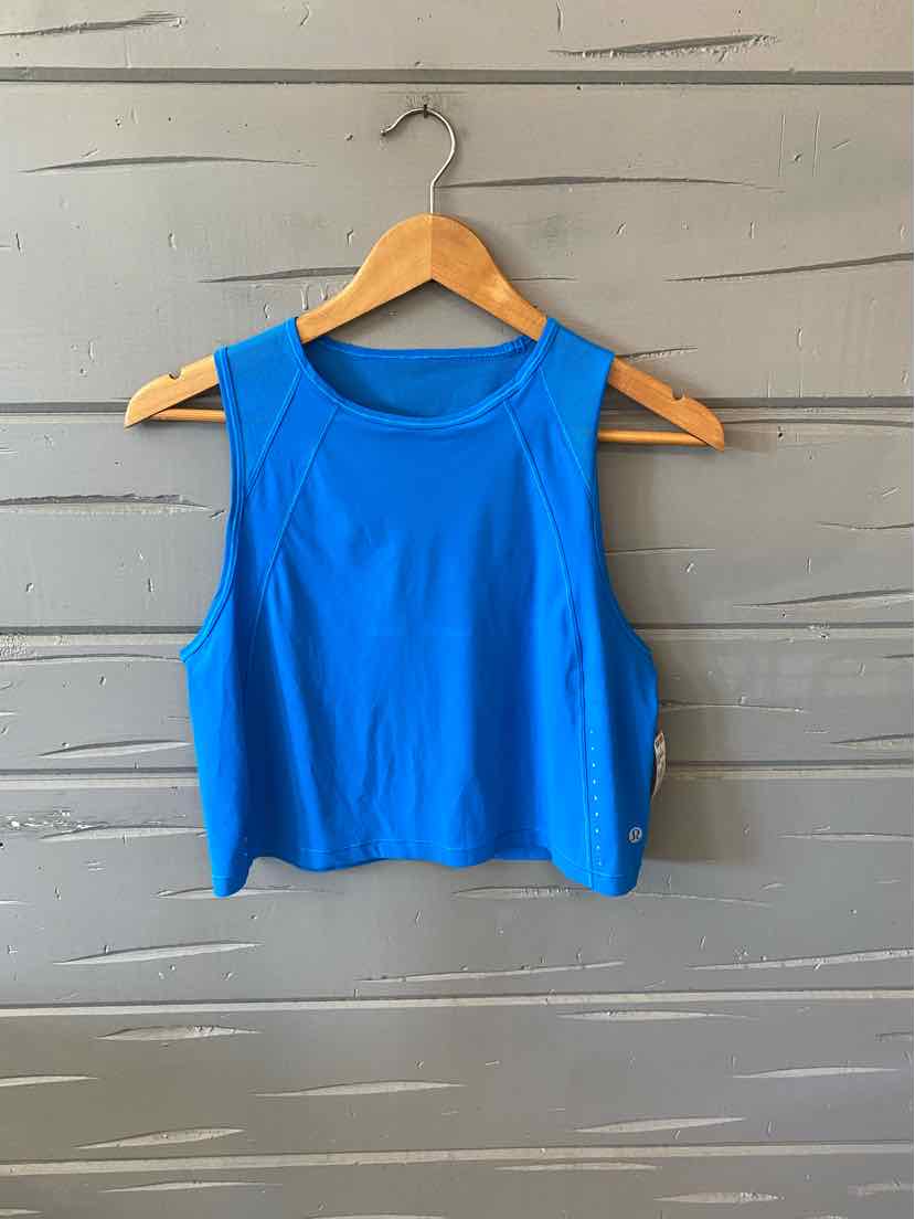 Bright blue sleeveless athletic crop top with wide shoulder straps and rounded neckline hanging on wooden hanger against.