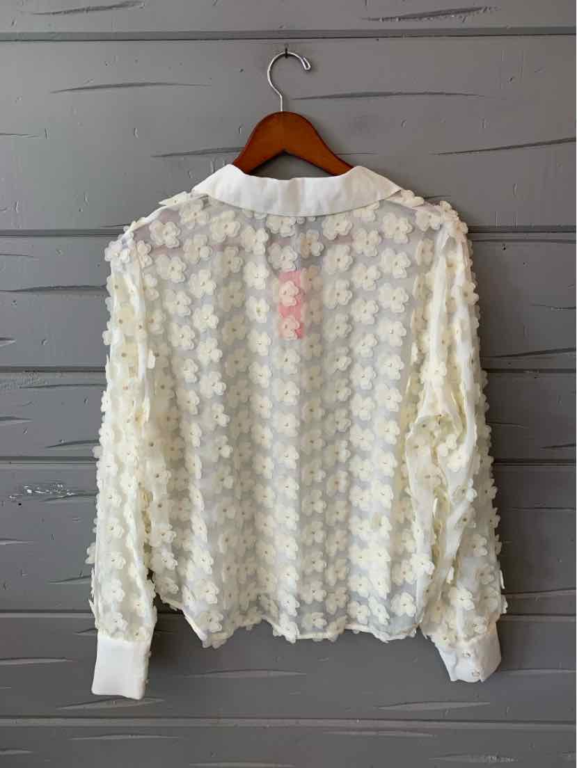White long-sleeve blouse with 3D floral lace overlay and ribbed collar and cuffs on wooden hanger.