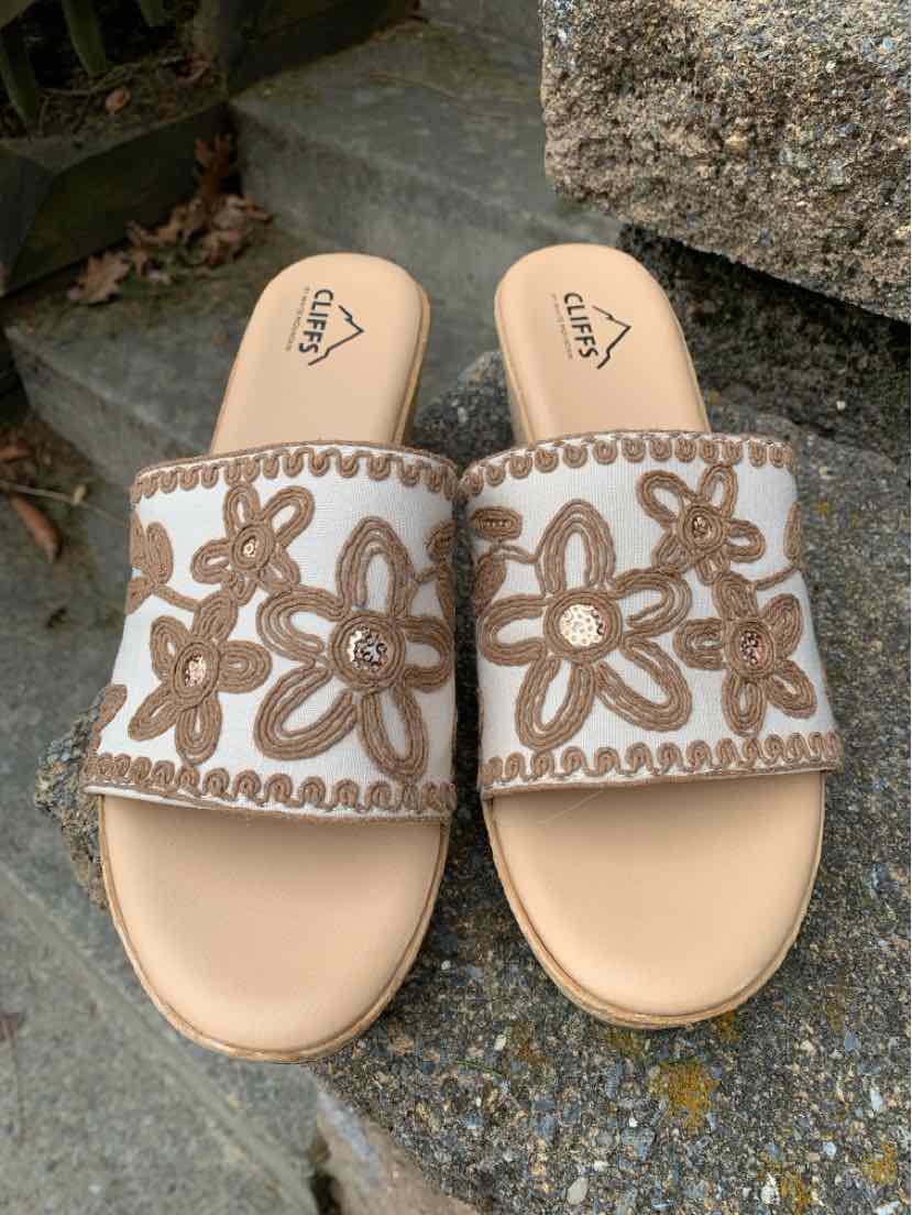 Beige slide sandals with wide white straps featuring intricate brown floral embroidery and cushioned footbeds.